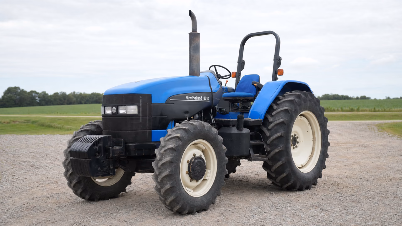 Blue New Holland 8010 tractor with an open station and four-wheel drive on a gravel farm drive.